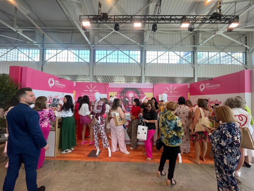 Visitantes recorren un stand de ProDominicana decorado en rosa, con exhibición de ropa y productos en una feria.